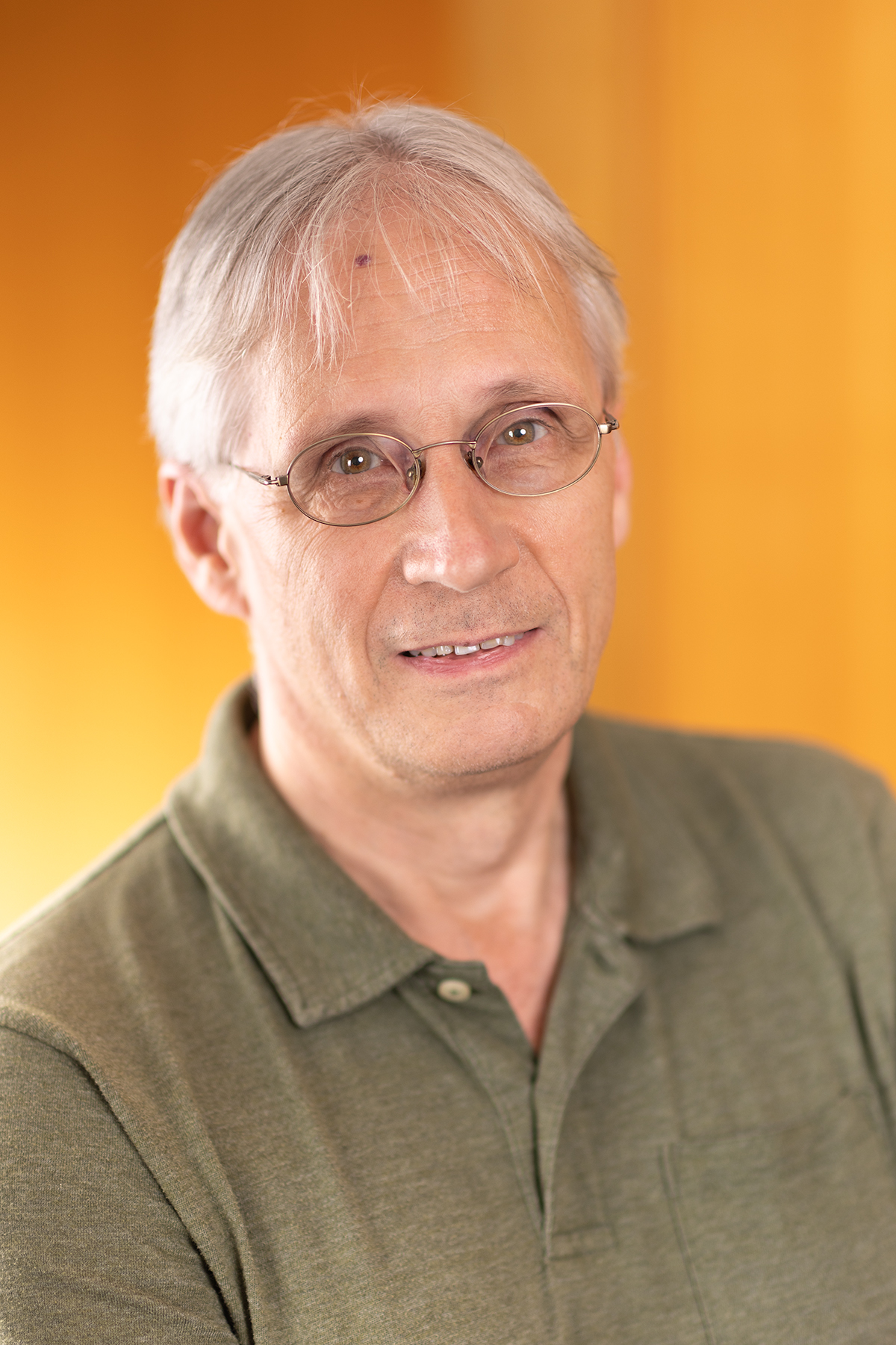 Professor Jon Abbatt, a white man in a green shirt,w ith white hair and glasses, smiles at the camera.