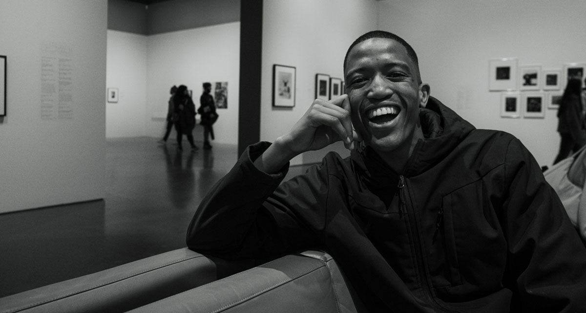 Black and white portrait of a young black man laughing in an art gallery.