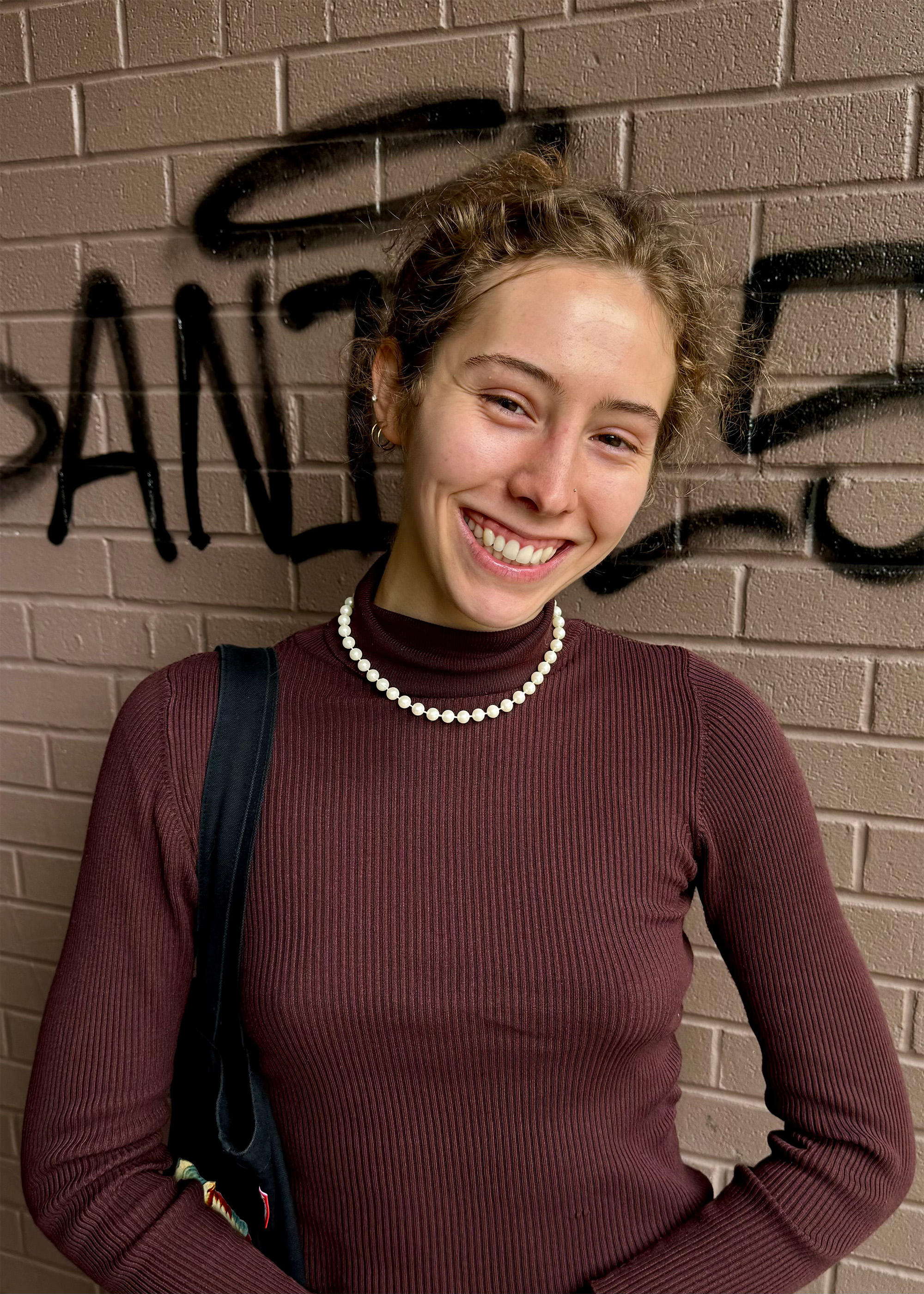 Chemistry student Anna Kirkland, a white woman with curly golden-brown hair and a brown top, smiles at the camera.