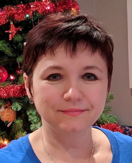 Head shot of a white woman with short brown hair standing in front of a Christmas tree.