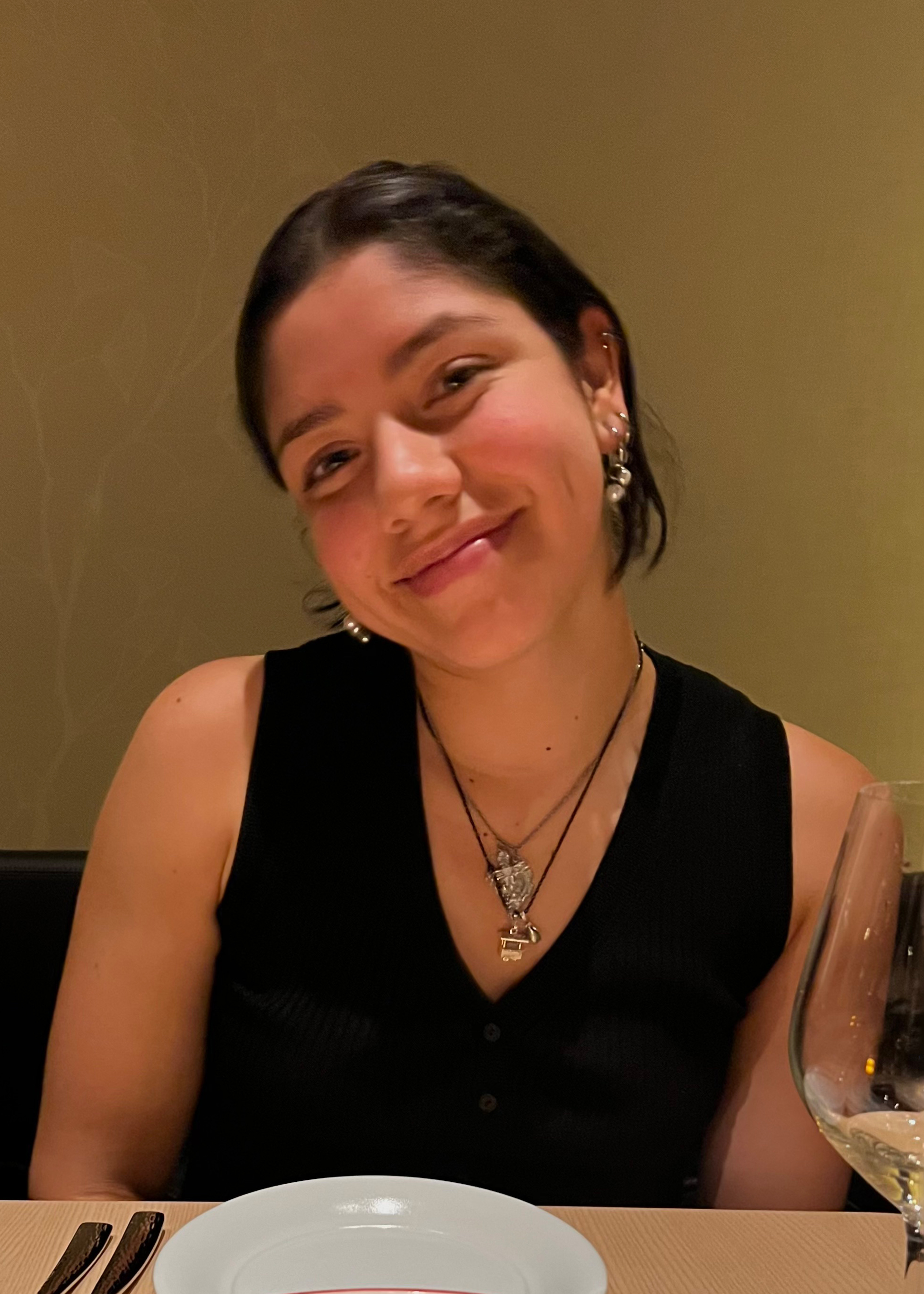 Chemistry student Maria Gendron, a brown woman with sleek hair pulled back from her face, sits a dinner table.