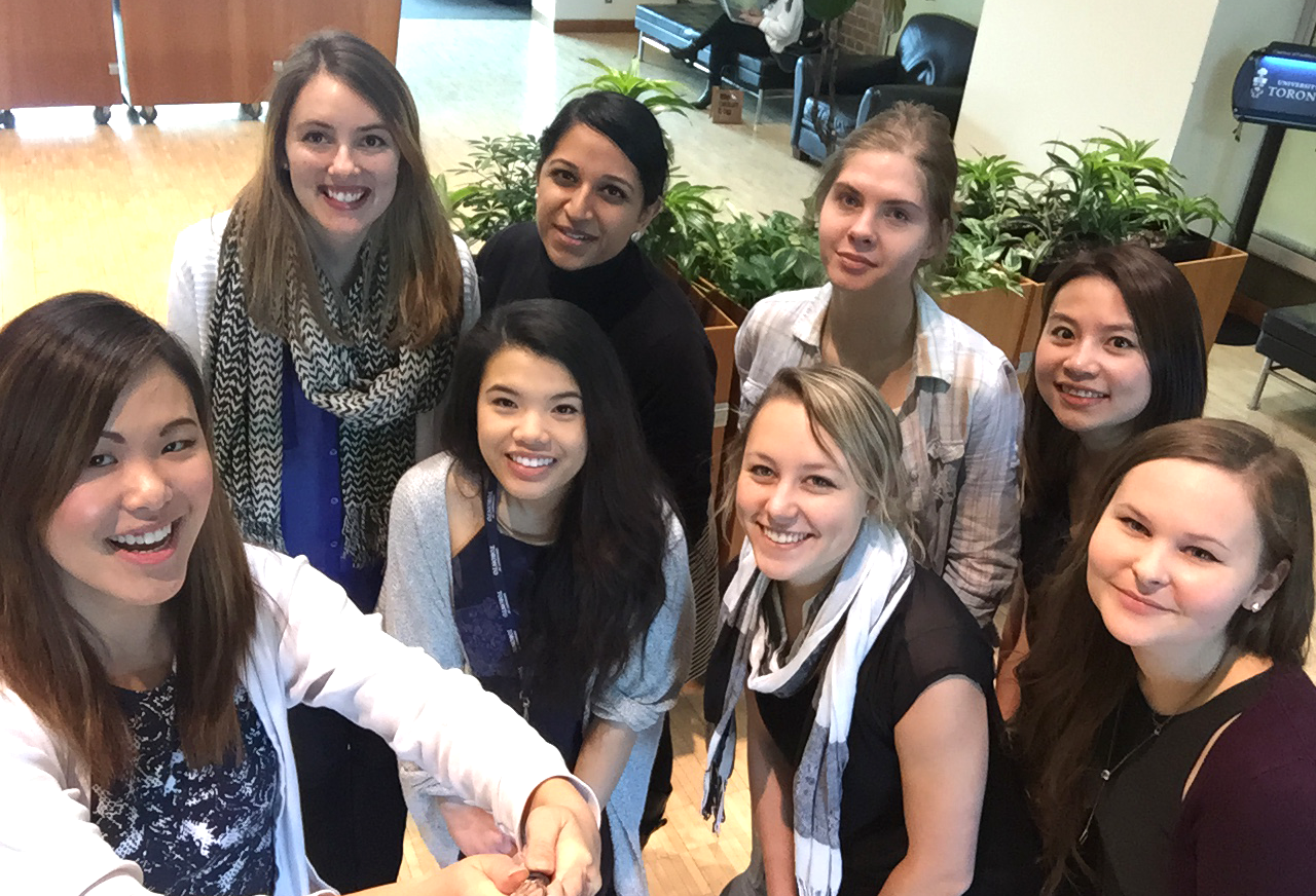 A group of chemistry students, all female-bodied, take a group shot with a selfie stick.