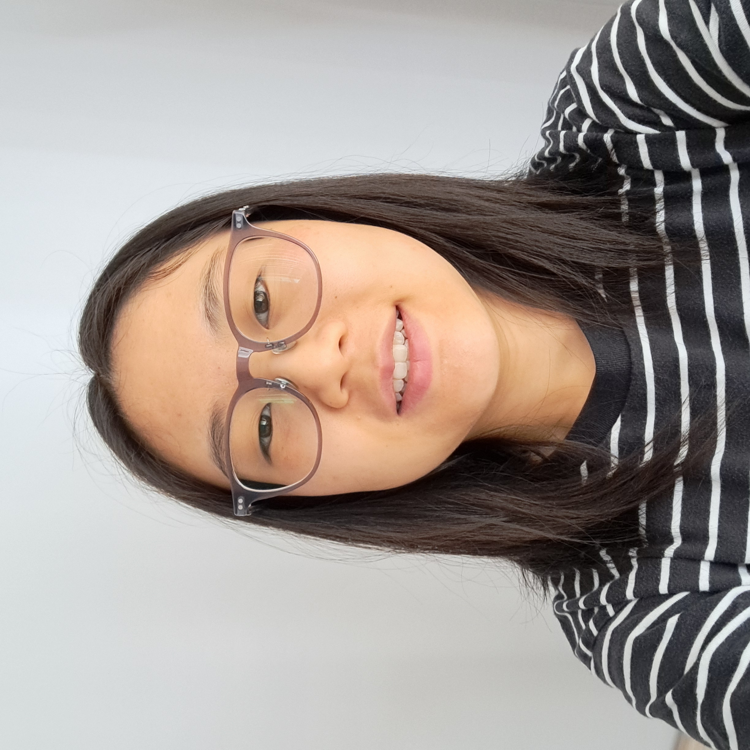 Head shot of a young asian woman with glasses and shoulder-length hair, wearing a striped black and white shirt