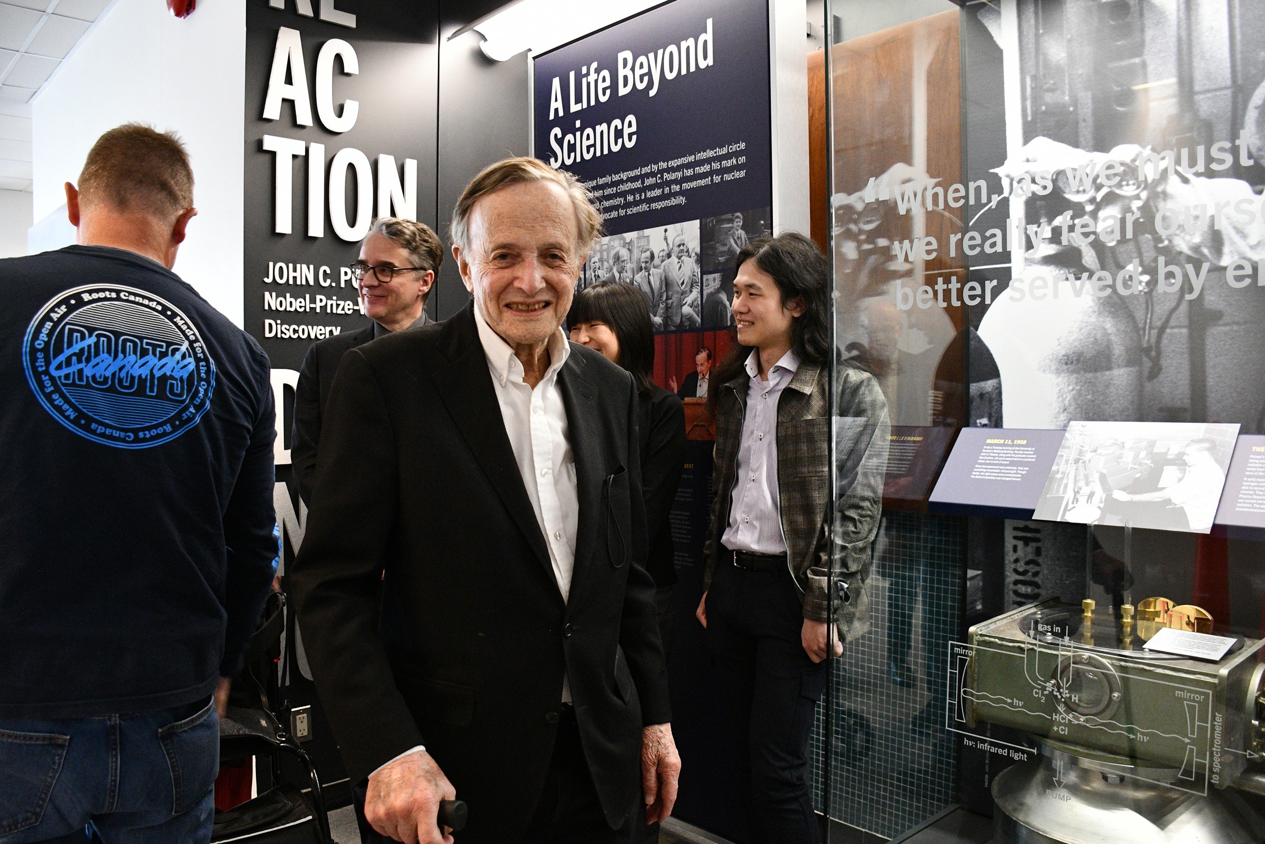 An older white man smiles at the camera from the corner of a display exhibit which read "A life beyond science." 