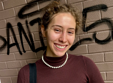 Chemistry student Anna Kirkland, a white woman with curly golden-brown hair and a brown top, smiles at the camera.