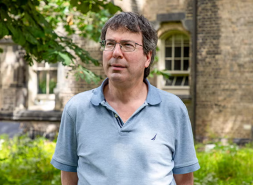 Portrait of Lewis Kay standing in front of a brick building.