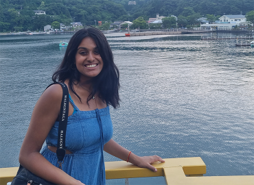 Chemistry student Devika Gopakumar smiles at the viewer from a boat, with green mountains behind her.