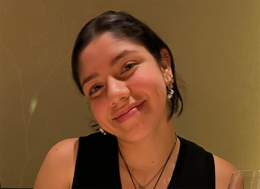 Chemistry student Maria Gendron, a brown woman with sleek hair pulled back from her face, sits a dinner table.