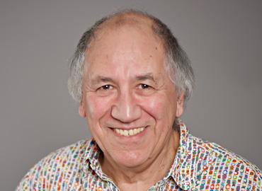 A white man in a colourful shirt smiles at the camera.
