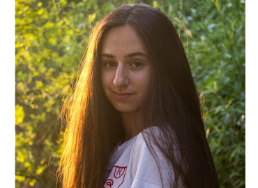 Chemistry student Sasha Maniaci looks sidelong at the camera with trees in the background.