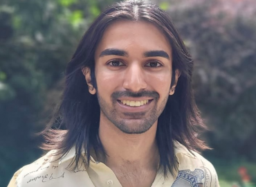 Head shot of a smiling South Asian man with shoulder-length brown hair.